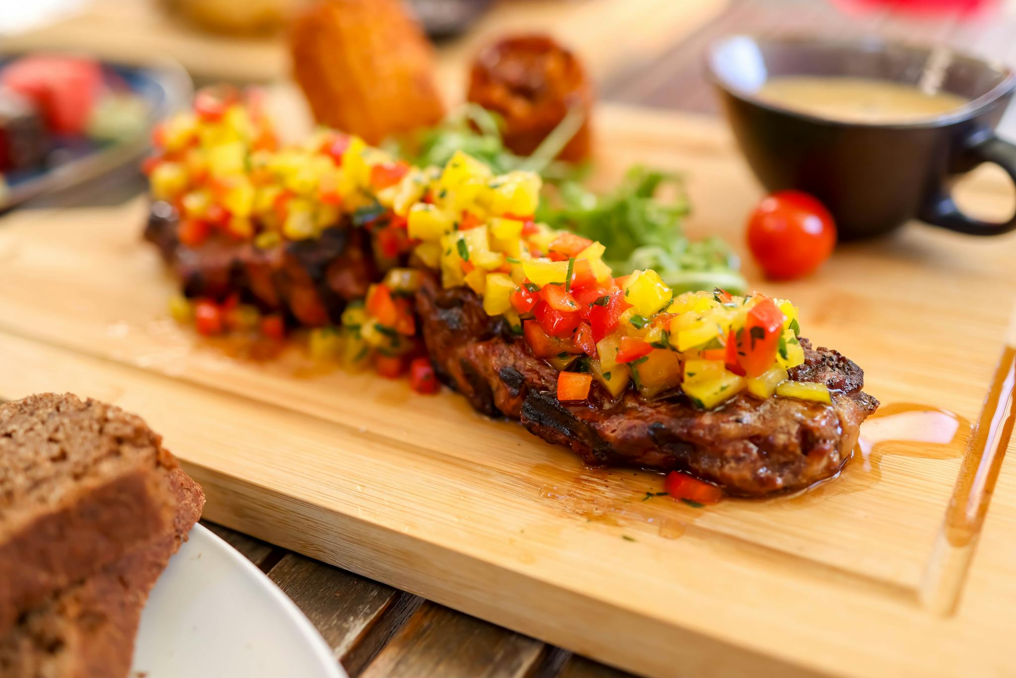 Close-up of a grilled steak topped with vibrant fruit salsa served on a wooden cutting board.